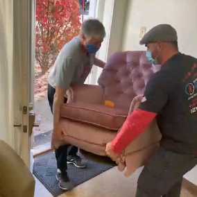 Two people bringing in a sofa in a room